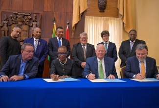 Prime Minister, Dr. the Most Hon. Andrew Holness (third left, backrow), and Science, Energy, Telecommunications and Transport Minister, Hon. Daryl Vaz (left, seated), observe as Acting Permanent Secretary in the Ministry of Science, Energy, Telecommunications and Transport, Olive Wilson Cross (second left, seated), Chief Executive Officer, Canadian Nuclear Laboratories Limited, Jack Craig (second right, seated), and President and Chief Executive Officer, Atomic Energy of Canada Limited, Fred Dermarker (right, seated), sign the Memorandum of Understanding (MOU) for advancing  nuclear technologies adoption in Jamaica. The signing took place at Jamaica House on Tuesday (October 22). Also observing are representatives from the International Centre for Environmental and Nuclear Sciences ICENS), University of the West Indies (UWI), Mona; Canadian Nuclear Laboratories Limited, and the High Commission of Canada in Jamaica.

