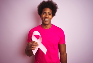 Man stands while holding pink ribbon symbolic of breast cancer awareness. 