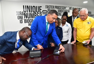 Prime Minister, Dr. the Most Hon. Andrew Holness (second left), is assisted by Programme Director for the National Identification System (NIDS), Dr. Warren Vernon, in the verification activity for the National Identification (ID) card, at the National Identification Registration Authority (NIRA) Personalisation Centre, located at Central Sorting Office in Kingston on November 15. Looking on (from third left) are Minister of Education, Skills, Youth and Information, Senator Dr. the Hon. Dana Morris Dixon; Executive Director of the Jamaica Council for Persons with Disabilities (JCPD), Dr. Christine Hendricks; Director General of the Planning Institute of Jamaica (PIOJ), Dr. Wayne Henry; and Minister of Justice, Hon. Delroy Chuck.