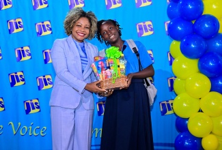 Minister of Education, Skills, Youth and Information, Senator Dr. the Hon. Dana Morris Dixon, presents Kamili Forrester of Goshen Primary in St. Elizabeth with a gift basket and backpack with stationery for first place in the essay category of the Jamaica Information Service (JIS) Heritage Competition, during the awards ceremony at the Terra Nova All-Suite Hotel in Kingston on December 10.