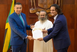 Prime Minister, Dr. the Most Hon. Andrew Holness (left), receives a letter of intent from Founder and Chief Executive Officer of the Amber Group, and Special Investment Envoy for Technology, Ambassador  Dushyant Savadia (right), formalising the Art of Living Foundation Jamaica and the Amber Group investment of US$5 million to advance critical initiatives in education, rural development, and prison rehabilitation across the country during a meeting at Jamaica House on December 13. At centre is internationally revered spiritual leader, humanitarian, and a peace ambassador and founder of the Art of Living Foundation, Gurudev Sri Sri Ravi Shankar. Ambassador Savadia is also an international teacher with the Art of Living Foundation.