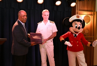 Port Authority of Jamaica (PAJ) President, Professor Gordon Shirley (left), presents a plaque to Captain of the ‘Disney Treasure’, Marco Nogara, during a Plaque Exchange Ceremony to mark the vessel’s maiden voyage to Jamaica on December 5. The vessel docked at the Falmouth Pier in Trelawny on Thursday, December 5. With them is the ship’s mascot, ‘Minnie’.

