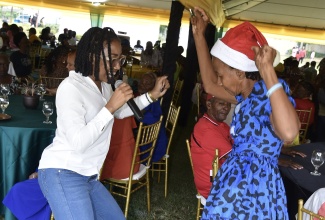 Media Personality Britney Clarke (left) dances with a senior citizen from the Vineyard Town Golden Age Home, at a Senior Citizen’s Treat held on the lawns of Jamaica House on Saturday (Dec.14). 

