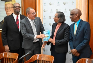 Minister of Health and Wellness, Dr. the Hon. Christopher Tufton (second left), presents a copy of his book, ‘Wild Flavours’, to Dean of the Faculty of Social Sciences at the University of the West Indies (UWI) Mona, Dr. Heather Ricketts (second right), during a Round-Table Policy Discussion held at the Mona campus in St. Andrew on Monday (December 9). Others (from left) are Director of the Sir Arthur Lewis Institute of Social and Economic Studies (SALISES), Professor Lloyd Waller (left), and Deputy Principal of the University, Dr. Tomlin Paul.