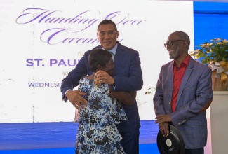 Prime Minister, Dr. the Most Hon. Andrew Holness (centre), shares a hug with Dorothy Scott, one of the new homeowners in the St. Paul’s Lane housing development in Tower Hill, St. Andrew. Occasion was the hand over of keys to 36 housing units in the development on Wednesday (December 11). Sharing the moment is Chairman of the National Housing Trust (NHT), Linval Freeman.