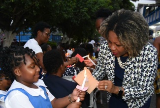 Minister of Education, Skills, Youth and Information, Senator Dr. the Hon. Dana Morris Dixon, lights a candle being held by Jessie Ripoll Primary School student, Zendeya Nelson, during the candlelight vigil for the late Principal, O