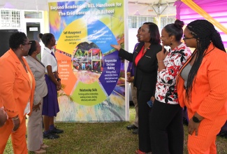 Acting Vice Principal at the St. Catherine based Enid Bennett High School and conceptualize of the Social and Emotional Learning (SEL) Programme, Latoya Bird-Miller (second right), points to a replica of a handbook, which contains the initiative, during the launch on January 30. Others (from left) are Acting Principal, Winsom Johnson; Education Officer with the Ministry of Education, Skills, Youth, and Information, Juanita Gordon Hunter; Head Girl, Kiara Mattis; Head Boy, Jeremy Peart; Senior Education Officer with the Ministry, Stephney Webb-Parker; and Supervisor for the Health and Family Life Education Department at the school, Talcea Hamilton.