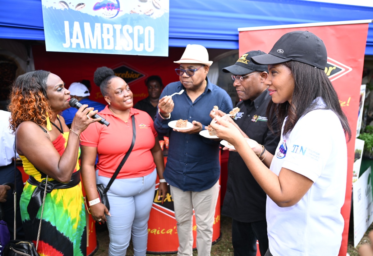 Minister of Tourism, Hon. Edmund Bartlett (centre), Minister of Industry, Investment and Commerce, Senator the Hon. Aubyn Hill, and Chair, Gastronomy Linkages Network, Nicola Madden-Greig (right), sample cinnamon cracker pudding with coffee sauce during the Jamaica Blue Mountain Coffee Festival at Hope Gardens in Kingston on Saturday (March 1). The treat was prepared using, among other ingredients, Excelsior brand crackers which are manufactured by Jamaica Biscuit Company. Looking on in anticipation of their reaction are event host and media personality, Jennifer “Jenny Jenny” Small, and Excelsior employee, Sharifa Rowe.