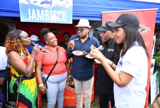 Minister of Tourism, Hon. Edmund Bartlett (centre), Minister of Industry, Investment and Commerce, Senator the Hon. Aubyn Hill, and Chair, Gastronomy Linkages Network, Nicola Madden-Greig (right), sample cinnamon cracker pudding with coffee sauce during the Jamaica Blue Mountain Coffee Festival at Hope Gardens in Kingston on Saturday (March 1). The treat was prepared using, among other ingredients, Excelsior brand crackers which are manufactured by Jamaica Biscuit Company. Looking on in anticipation of their reaction are event host and media personality, Jennifer “Jenny Jenny” Small, and Excelsior employee, Sharifa Rowe.

