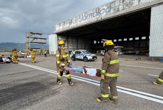 Members of the Jamaica Fire Brigade (JFB) extract a “victim” from the scene of a staged plane crash to the medical triage area during a simulation exercise at the Norman Manley International Airport in Kingston.

