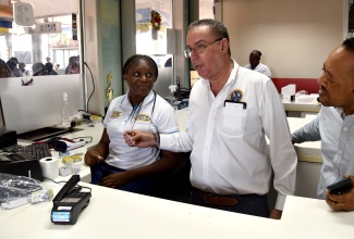 Minister of Science, Energy, Telecommunications and Transport, Hon. Daryl Vaz (centre), examines a new SmartFare card shown to him by Jamaica Urban Transit Company (JUTC) Revenue Agent, Alecia Blackwood.  Looking on is the Transport Authority (TA) Managing Director, Ralston Smith. The JUTC launched its new SmartFare system on Tuesday (March 4) at the Half-Way Tree Transport Centre in Kingston.