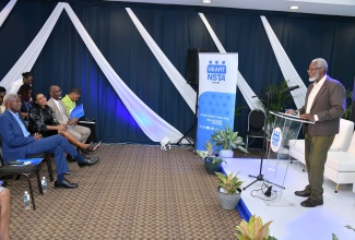 University of the West Indies (UWI) Lecturer, Professor Disraeli Hutton, delivers the keynote address at the HEART/NSTA Trust’s Technical and Vocational Education and Training (TVET) Research Symposium at the UWI Regional Headquarters in Kingston on Wednesday (March 12). Listening in the audience are HEART/NSTA Trust Board Chairman, Professor Alvin Wint (left), Managing Director of the HEART/NSTA Trust, Dr. Taneisha Ingleton (second left) and other participants.

