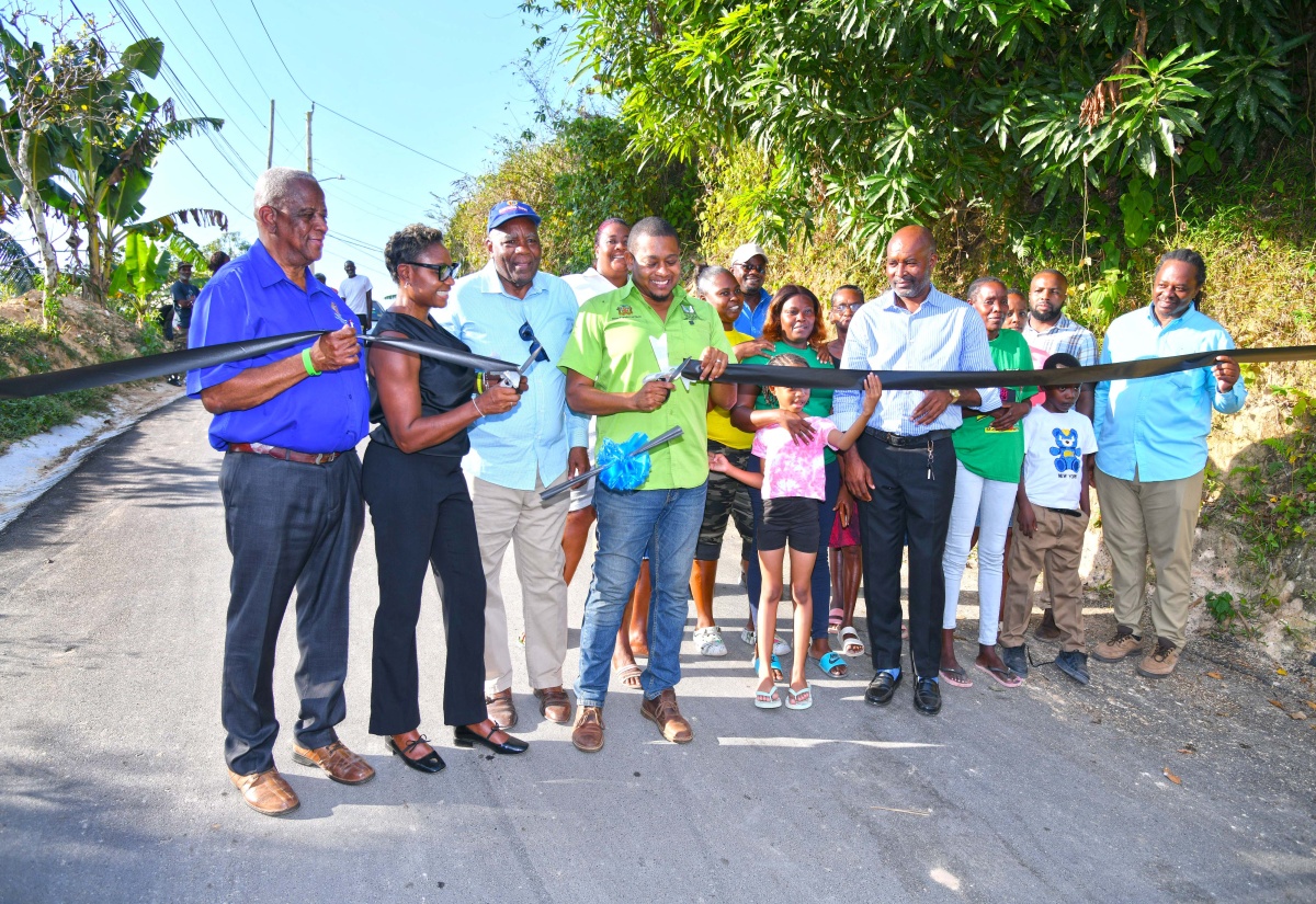 Minister of Agriculture, Fisheries and Mining, Hon. Floyd Green (4th left), cuts the ribbon to officially open the Mount Olive Farm Road in St. Andrew on Wednesday (March 26). Joining him (from left) are State Minister in the Ministry, Hon. Franklin Witter; Member of Parliament for West Rural St. Andrew and State Minister in the Ministry of National Security, Hon. Juliet Cuthbert-Flynn; Councillor for the Lawrence Tavern Division, John Myers; Chief Executive Officer (CEO) of the Rural Agricultural Development Authority (RADA), Garnet Edmondson; and members of the community.