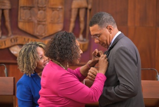 Prime Minister, Dr. the Most Hon. Andrew Holness, is affixed with a pin commemorating International Women’s Day by Minister of Culture, Gender, Entertainment and Sport, Hon. Olivia Grange, during a special edition of the post-Cabinet press briefing in observance of the Day at Jamaica House on Tuesday (March 4). Looking on is Minister of Education, Skills, Youth and Information, Senator Dr. the Hon. Dana Morris Dixon. International Women’s Day will be observed on March 8.