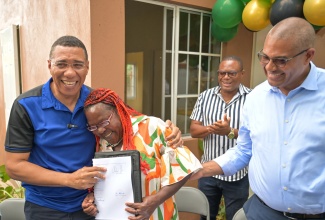 Prime Minister, Dr. the Most Hon. Andrew Holness (left), hugs a grateful Norma Williams as he hands her a social contract to a new housing unit under the New Social Housing Programme (NSHP), in Greenvale, Manchester, on Friday, March 7. Sharing the moment is Manchester North Western Member of Parliament, Mikael Phillips (right).

