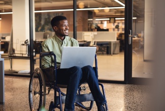 Smiling man with a disability in the workplace using a laptop in a wheelchair