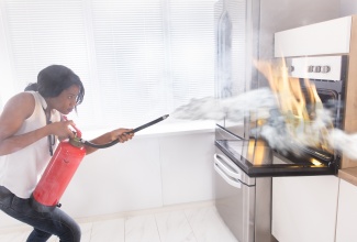 Woman using fire extinguisher to stop fire coming from oven in kitchen