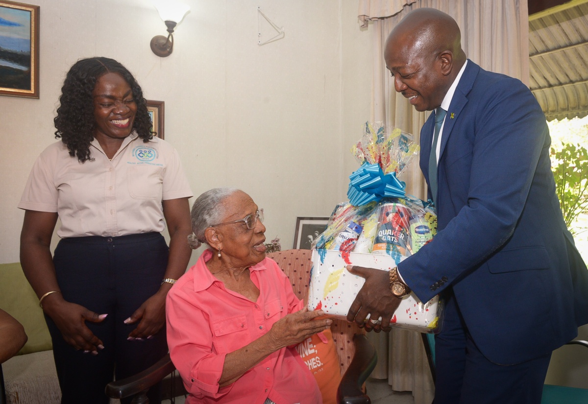 Minister of Labour and Social Security, Hon. Pearnel Charles Jr., presents a gift basket to centenarian, Mollie Berkley, during a visit to her home in Liguanea, St. Andrew, on Tuesday (May 20). The visit was a part of activities marking National Centenarians’ Day. Sharing the moment is Executive Director, National Council for Senior Citizens (NCSC), Cassandra Morrison.