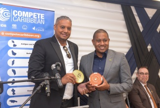 Minister of Agriculture, Fisheries and Mining, Hon. Floyd Green (right), receives samples of canned conch from Jamaica Conch Cluster (JCC) Lead, Roderick Francis, during Thursday’s (May 29) closing-out ceremony for the two-year JCC Project at the Inter-American Development Bank (IDB) Kingston office. In the background is Canada’s High Commissioner to Jamaica, His Excellency Mark Berman.