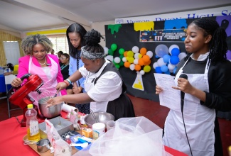 Minister of Education, Skills, Youth and Information, Dr. the Hon. Dana Morris Dixon (left), tries her hand at baking a cake with the assistance of student, Judia Walker (second right), during a visit to the Victor Dixon High School in Mandeville, Manchester, on Thursday (May 2). Member of Parliament, Manchester Central, Rhoda Moy Crawford, looks on. At right, student Kalee Hinds, provides instruction on how to bake the cake.

