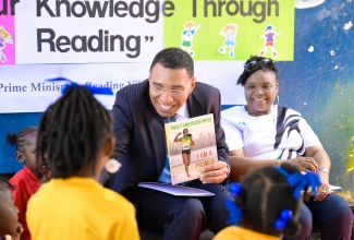 Prime Minister, Dr. the Most Hon. Andrew Holness, shows students of Seaward Primary and Infant School the cover of the book ‘I am a Promise’ by Shelly-Ann Fraser-Pryce, during Read Across Jamaica Day activities at the institution in St. Andrew on May 6. He is joined by Principal of the school, Arlene Reid.