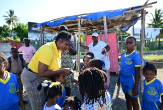 Chair of the National Child Month Committee, Nicole Patrick Shaw (left), distributes tokens and stickers to students from the St. Thomas Hill View Kinder-Prep School, as part of children's day activities on May 16, in Morant Bay.