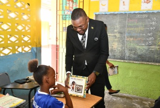 Minister without Portfolio in the Ministry of Economic Growth and Job Creation with responsibility for Works, Hon. Robert Morgan, shows student Nerricia Kalisa Vernon illustrations in the book ‘My Big Family’ during a reading session at Rock River Primary School.  The Minister participated in Read Across Jamaica Day activities at the institution in Clarendon on Tuesday (May 6).

