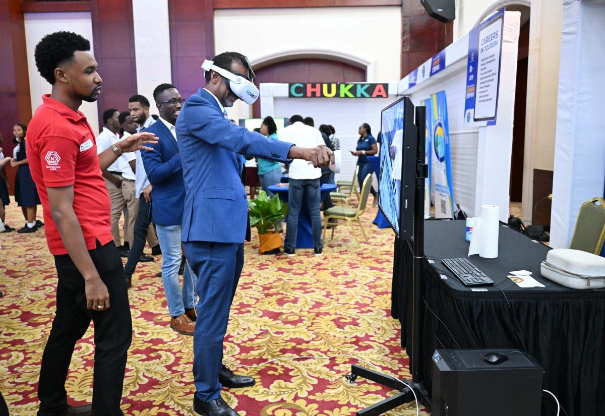 Executive Director, Tourism Enhancement Fund (TEF), Dr. Carey Wallace (right), experiences virtual reality during the Jamaica Centre for Tourism Innovation (JCTI) Tourism Career Expo 2025, held on Thursday, May 1, at the Montego Bay Convention Centre in Rose Hall, St. James. Observing the demonstration is Alec Afflick, Technical Officer for NovaCore Labs.


