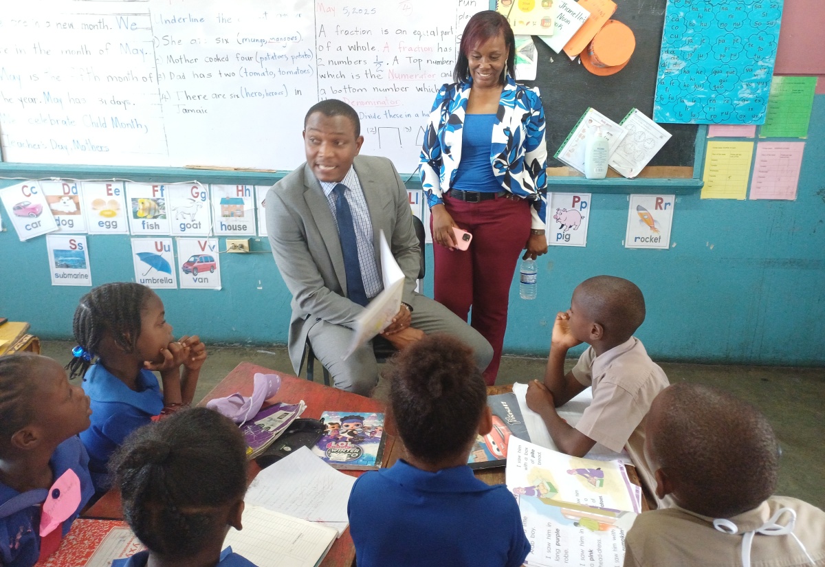 President of the Jamaica Teachers’ Association (JTA), Dr. Mark Smith (left, seated), reads to students at the Hayes Primary and Infant School in Clarendon, during the recent observance of Read Across Jamaica Day at the institution.  Also pictured is teacher at the Vere Technical High School, Carla Pitter.

