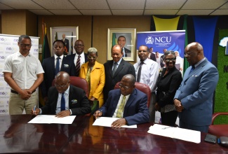 Chief Executive Officer at the National Environment and Planning Agency (NEPA), Leonard Francis (seated left),and President of the Northern Caribbean University (NCU), Dr. Lincoln Edwards (seated right), sign a Memorandum of Understanding (MOU) to deepen collaboration between the entities on environmental research, natural resource management and sustainable development. The signing took place at NEPA’s Caledonia Avenue office in Kingston on Thursday (May 15). Looking on (standing from left) are Deputy Chairman of the Natural Resources Conservation Authority (NRCA)/Town and Country Planning Authority (TCPA), Christopher Whyms-Stone; Director for Information and Communications Technology (ICT) at NEPA, Othniel Kidd; Director of Planning, Projects Monitoring Evaluation and Research at NEPA, Ainsworth Carroll; Manager for Planning, Monitoring Evaluation and Research, Marvette Brown; Dean, College of Natural and Applied Sciences, Allied Health and Nursing, NCU, Dr. Vincent Wright; Assistant Professor, Biology, Chemistry and Environmental Sciences Department, NCU, Alston Miller; Director of Corporate/Community Relations and Strategic Partnership Department, NCU, Nadeen Campbell; and Associate Director, Community Relations and Strategic Partnerships Department and Legal Advisor, NCU, Victor Cummings.