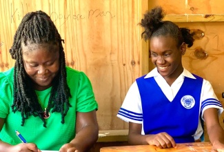 Felicia Bethune (left) takes notes for her daughter, Daejhanae Lumsden, during a class at Yallahs High School in St. Thomas. Ms. Bethune serves as a shadow for the grade-nine student, who suffers from developmental delay, which affects her fine motor skills.

