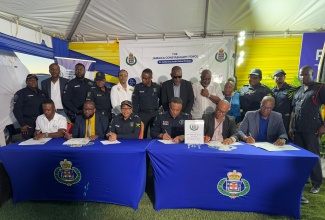 Permanent Secretary in the Ministry of National Security, Ambassador Alison Stone Roofe (fifth left, standing), and Commanding Officer for Jamaica Constabulary Force (JCF) Area Five, Assistant Commissioner of Police (ACP) Christopher Phillips (sixth left, standing), and other stakeholders observe as the Presidents of four new neighbourhood watches in Hellshire, St. Catherine, sign the Neighbourhood Watch Memorandum of Understanding (MOU). The occasion was a joint launch at the Sandhills Vista Community Centre in Hellshire, St. Catherine, on Saturday (May 10).

