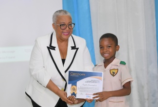 Managing Director of the Jamaica Stock Exchange (JSE), Dr. Marlene Street-Forrest, presents top student in the entity’s Primary and Preparatory Schools Stock Market Game for Month 2, Zayden Cunningham, with his certificate at today’s (May 16) awards ceremony for students who participated in the competition, at the JSE, downtown Kingston.