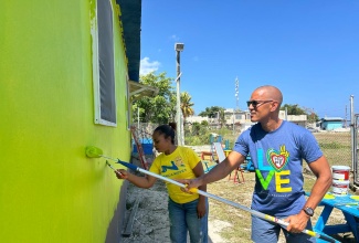 General Manager of Sandals Montego Bay, Christopher Elliott (right), and Principal of the Whitehouse Early Childhood Centre, Ann Blake-Reid (left), paint the exterior of the institution during Labour Day activities on Friday, May 23 in St James.

