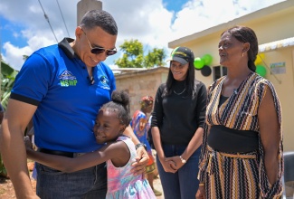 Prime Minister, Dr. the Most Hon. Andrew Holness, receives a warm hug from Kellisa Green, granddaughter of Karen Campbell (right), who is the recipient of a new home under the New Social Housing Programme (NSHP). The three-bedroom unit was handed over in Cedar Grove, Manchester on Friday (May 9). Sharing the moment is Member of Parliament for Manchester Central, Rhoda Moy Crawford.