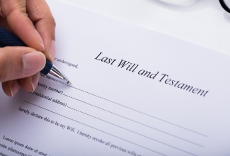 Close-up of a person's hand filling Last Will and Testament Form