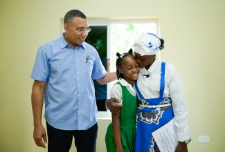 Prime Minister, Dr. the Most Hon. Andrew Holness (left) looks on as New Social Housing Programme (NSHP) beneficiary, Patrica Rowe (right) embraces her granddaughter, Asantiwa Gordon. Occasion was the handover ceremony for Ms. Rowe