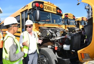 Science, Energy, Telecommunications and Transport Minister, Hon. Daryl Vaz (right), explains the components of the engine in one of the new units that will be used in the rural school bus system to Finance and the Public Service Minister, Hon. Fayval Williams. Occasion was the arrival of the first 25 school buses at Kingston Wharves on Tuesday (June 24).


