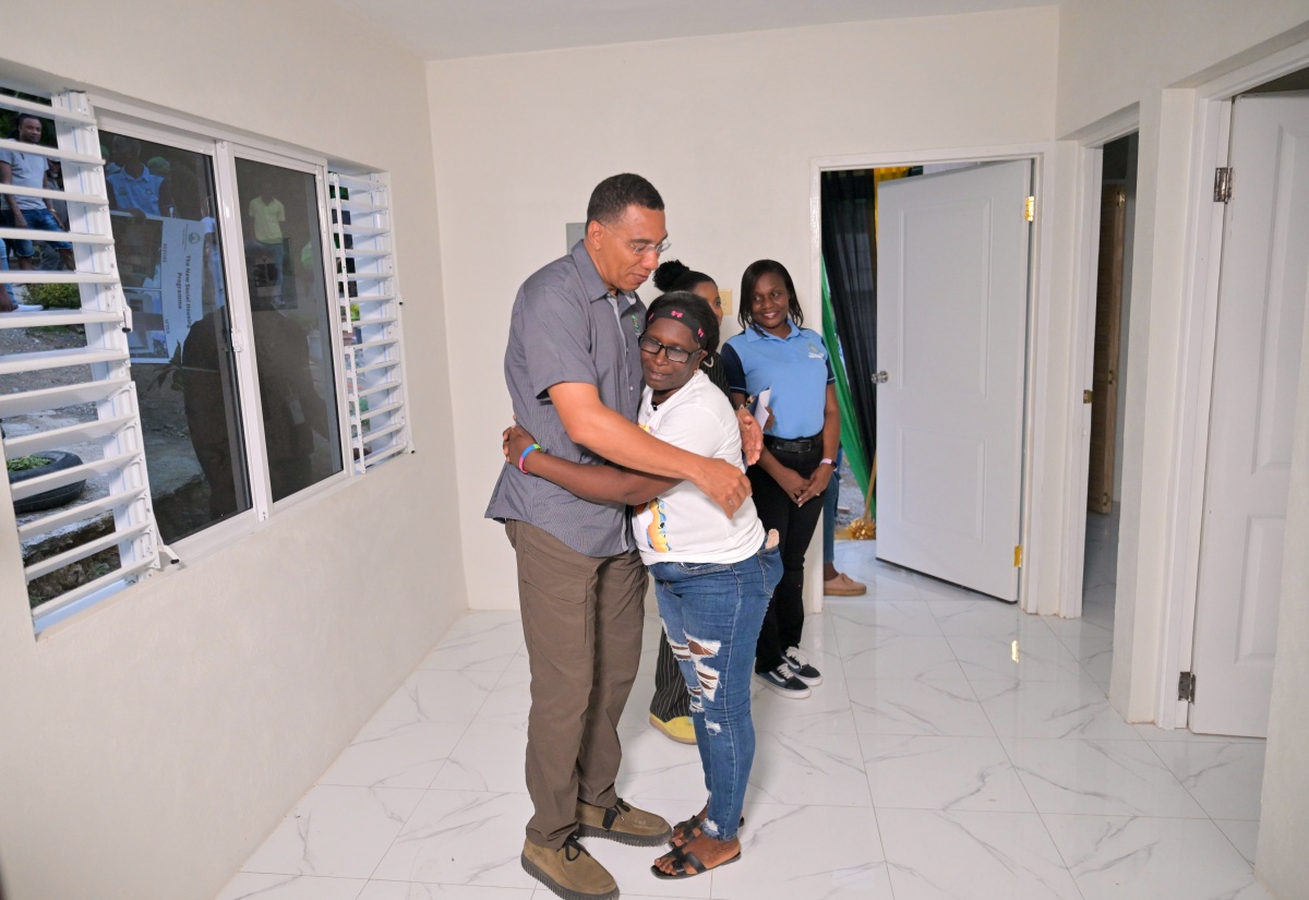 Prime Minister, Dr. the Most Hon. Andrew Holness (left), embraces New Social Housing Programme (NSHP) beneficiary, Shirley Bennett, following the handover of her new two-bedroom home during a ribbon-cutting ceremony on Thursday (June 19) in Style Hut, Port Morant, St. Thomas. In the background are Permanent Secretary in the Ministry of Economic Growth and Job Creation, Arlene Williams (right), and Member of Parliament for St. Thomas Eastern, Dr. Michelle Charles.