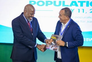 Minister of Health and Wellness, Dr. the Hon. Christopher Tufton (right), is presented with a copy of the National Population and Sustainable Development Policy (NPSDP), by Planning Institute of Jamaica (PIOJ) Director General, Dr. Wayne Henry, during the launch on World Population Day, Friday (July 11) at AC Hotel by Marriott in Kingston.