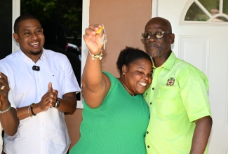 Minister of Local Government and Community Development, Hon. Desmond McKenzie (right), embraces beneficiary, Shawya Farquharson, after handing over the keys to her newly constructed $6.7 million housing unit, provided under the Indigent Housing Programme in Brompton, St. Elizabeth, on Friday (July 4). Looking on is Minister of Agriculture, Fisheries and Mining and Member of Parliament for St. Elizabeth South Western, Hon. Floyd Green.