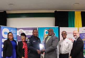 Director General of Road Traffic at the Island Traffic Authority (ITA), Colonel Daniel Pryce (third right), presents a tablet computer to Head of the Jamaica Constabulary Force (JCF) Public Safety and Traffic Enforcement Branch (PSTEB), Assistant Commissioner of Police (ACP) Dr. Gary McKenzie, during the National Road Safety Council (NRSC) meeting at the Courtleigh Hotel & Suites in Kingston on June 26.  Others (from left) are Advisor, Non-Communicable Disease and Mental Health, Pan American Health Organization (PAHO), Dr. Patrice Lawrence-Williams; NRSC Executive Director, Paula Flecther, and Vice Chairman, Dr. Lucien Jones; and PAHO/WHO (World Health Organization) Representative for Jamaica, Bermuda and the Cayman Islands, Ian Stein.

