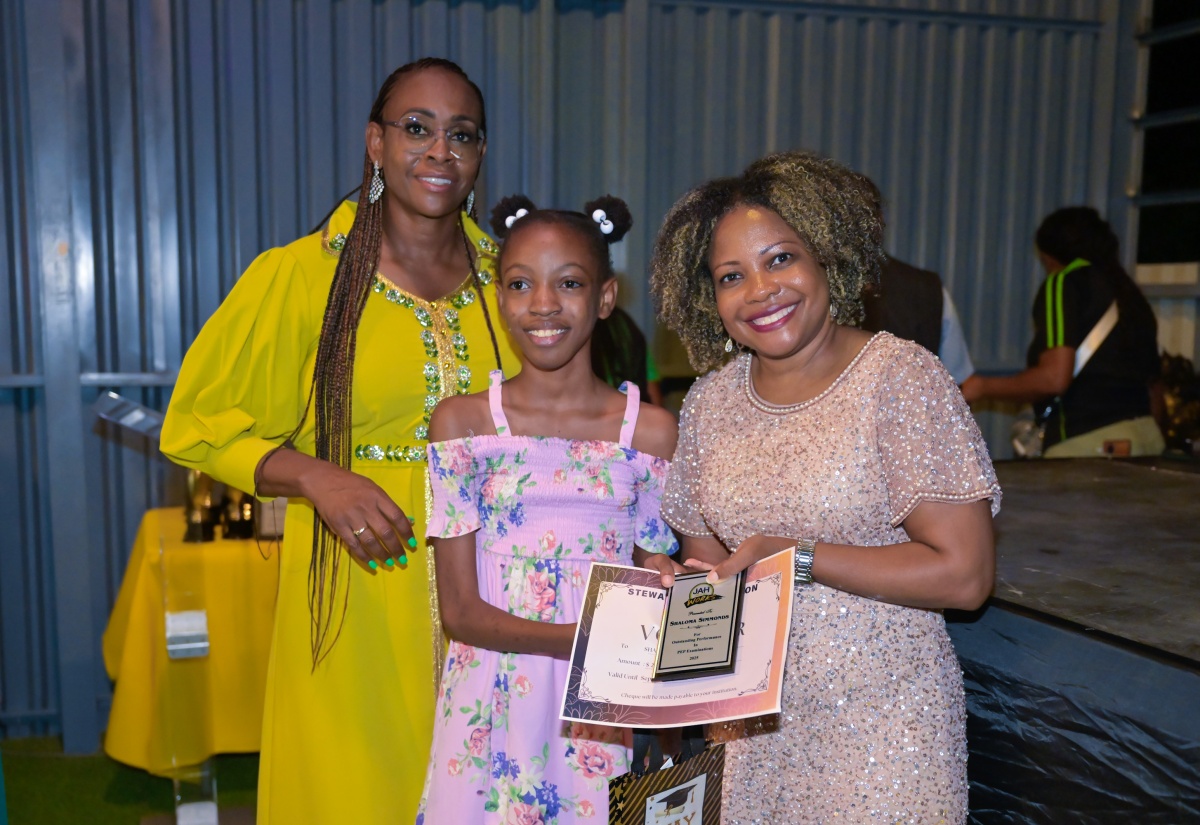 Minister of Education, Skills, Youth and Information, Senator Dr. the Hon. Dana Morris Dixon (right) makes a presentation to Shaloma Simmonds (centre) for outstanding performance in her Primary Exit Profile (PEP) examinations, while Member of Parliament (MP) for St. Andrew East Rural, the Most Hon. Juliet Holness, shares the moment. Shaloma was among 91 students recognised at the 2025 PEP awards dinner hosted by Mrs. Holness at the Hillside City Centre in Lower Halls Delight on Thursday (July 31).