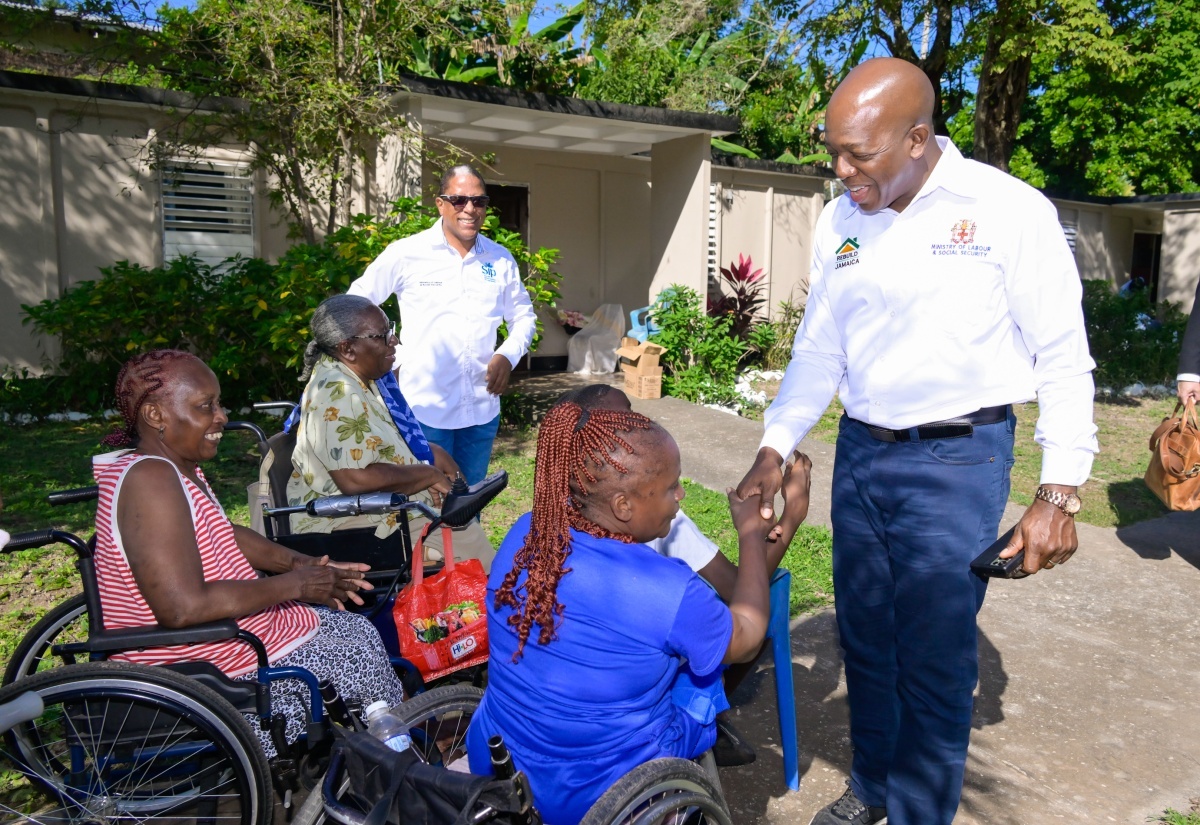 Minister of Labour and Social Security, Hon. Pearnel Charles Jr (right), engages with residents of Cheshire Village, during a visit to the community for disabled persons in St. Andrew last December to hand over care packages.  Looking on is State Minister, Dr. the Hon. Norman Dunn.
