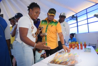 Jamaica Network of Rural Women Producers (JNRWP) member, Latoya Rattray-Ellis (left), showcases products produced by members of the JNRWP to Minister of Agriculture, Fisheries and Mining, Hon. Floyd Green (centre) and Jamaica Agricultural Society (JAS) Chief Executive Officer (CEO), Derron Grant, at the 71st staging of the Denbigh Agricultural, Industrial and Food Show, at the Denbigh Showground in May Pen, Clarendon, on Saturday (August 2).
