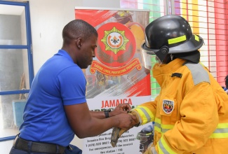 Corporal Kerol Allen of the Jamaica Fire Brigade (left) assists a resident of the Mount Olivet Boys’ Home in Manchester with trying on bunker gear, during the recent Back-to-School Treat and Career Expo hosted at the institution by the Jamaica Information Service (JIS)

