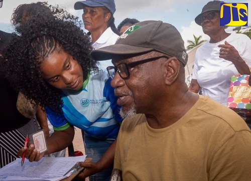 Records and Information Management (RIM) Officer at the National Council for Senior Citizens (NCSC), Nesa Lawrence (left), assists visually impaired senior citizen, Karl Morrison, in registering to access services, at an Ageing Fair held at Emancipation Park in St. Andrew on Thursday (Sept. 11).