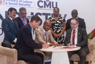 Caribbean Maritime University (CMU) President, Professor Andrew Spencer (centre, seated), and ECO Canada President and Chief Executive Officer, Kevin Nilsen (left, seated), sign documents formalising an academic partnership forged between the entities that will facilitate local and Caribbean-wide upskilling and training in the environmental sector. The occasion was the opening ceremony for the CMU’s Industry/Academics Conference 2025 at The Jamaica Pegasus hotel in New Kingston on Wednesday (October 1). Looking on are High Commissioner of Canada to Jamaica, His Excellency Mark Berman (right, seated), and (from left, standing) are ECO Canada Vice President of Professional Services, Dr. Yogendra Chaudhry, and Director of Professional Services, Dr. Devant Maragh; CMU Registrar, Keisha Walker, and Deputy to the President, Professor Ibrahim Ajagunna.

