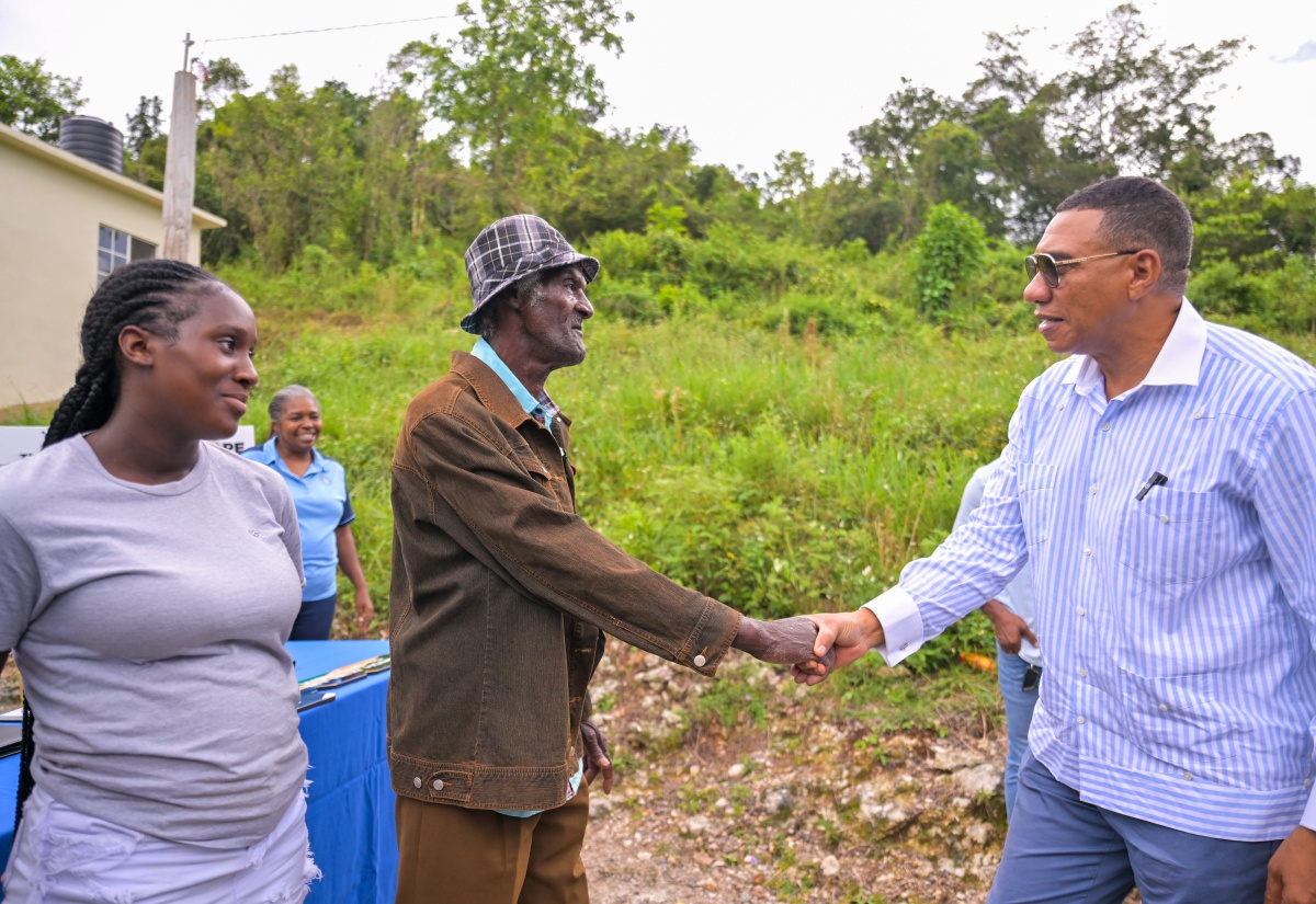 Prime Minister, Dr. the Most Hon. Andrew Holness (right) greets beneficiary Neville Barrett (centre) on arrival at the handover ceremony for a one-bedroom house in St. Dacres, St. Ann on October 10 under the Government’s New Social Housing Programme (NSHP).  Sharing in the moment is Janile Rose, niece of Mr. Barrett.