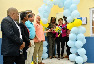 Regional Director at the Southern Regional Health Authority (SRHA), Michael Bent (left) and Parish Manager for Manchester Health Services, Sadia Ferguson (second left), look on as Medical Director of Won by One to Jamaica (WBOTJ), Beth Fellers (second right), cuts the ribbon at the recent official opening and handover of the new Harmons Health Centre in Manchester. The project was undertaken by the United States-based non-profit organisation at a cost of $14 million. Ms. Fellers is assisted by Senior Public Health Nurse, Maxine Isaacs (third right), and community member, Kenton Gordon (right). Chairman of WBOTJ, Rich Mitchell (third left); and Executive Director, Dr. Bryan Fellers, also look on.